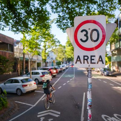 a street in Fitzroy with a 30km speed limit sign in the foreground and cyclists using the street in the background.