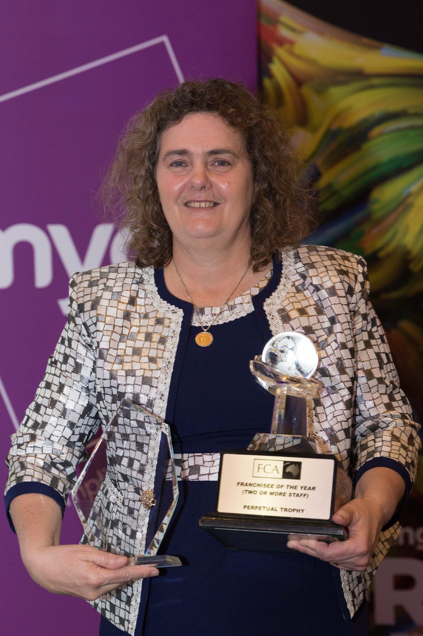a women holding pointing to her award posing for a photo