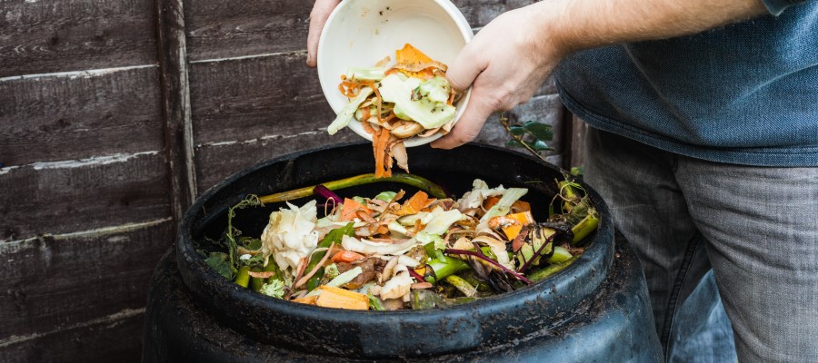Person emptying a bowl of colourful food scraps into a compost bin. Bin is already at the brim with existing food scraps.