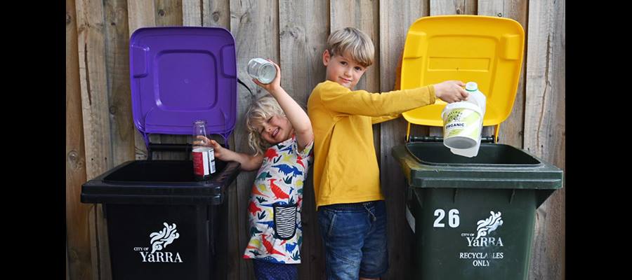 Young boy and girl separating glass from plastic items using purple and yellow recycling bins