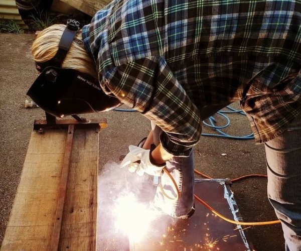 Person in a plaid shirt wearing a protective face shield while using a power tool.