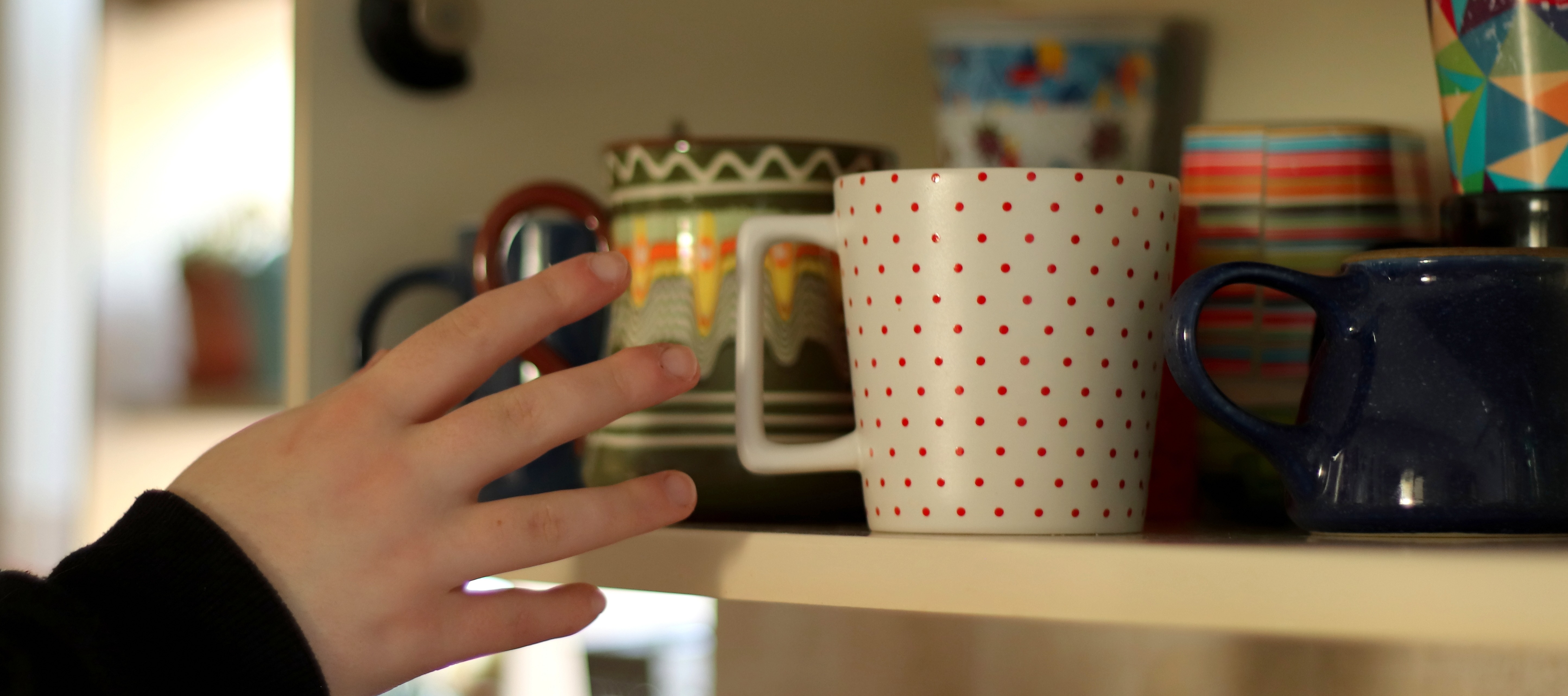 a hand reaches for a mug in a kitchen cupboard