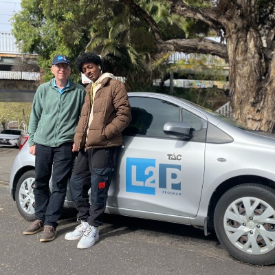 A volunteer driving mentor and their mentee standing in front of a car